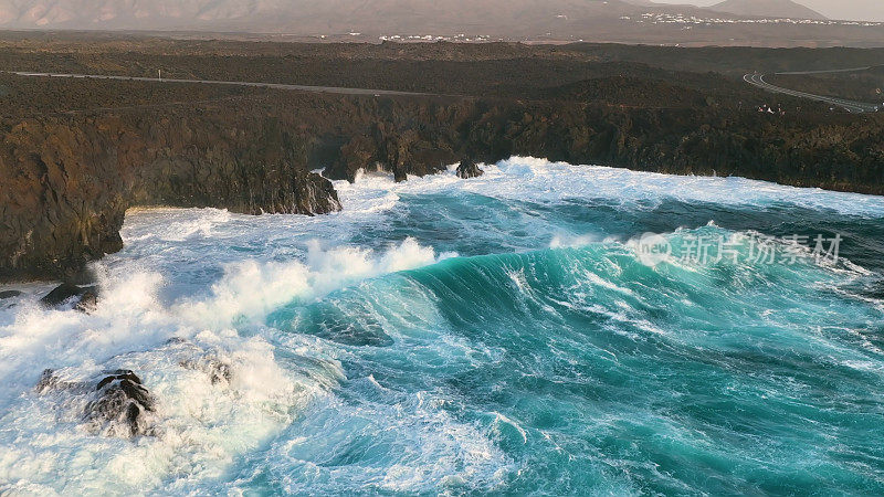 4K航拍慢镜头，湛蓝的海洋和巨大的海浪撞击岩石悬崖，溅起浪花和白色泡沫。兰萨罗特岛。西班牙加那利群岛