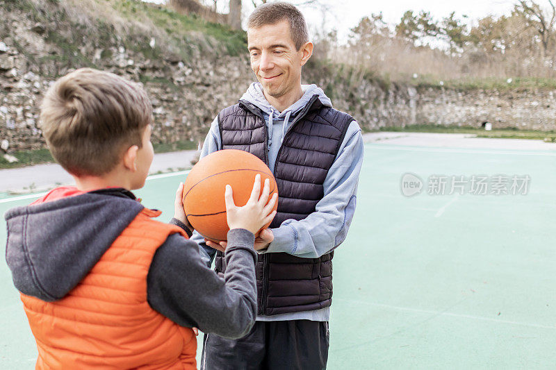 父亲和儿子在球场上打篮球，教小球员。幸福和健康的家庭快乐。户外运动。