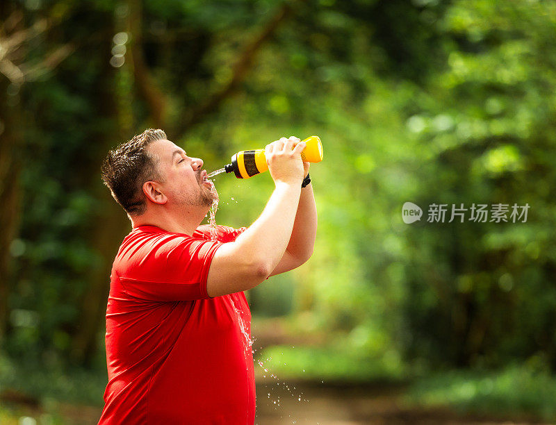 疲惫的男性慢跑者在森林里从瓶子里喷水