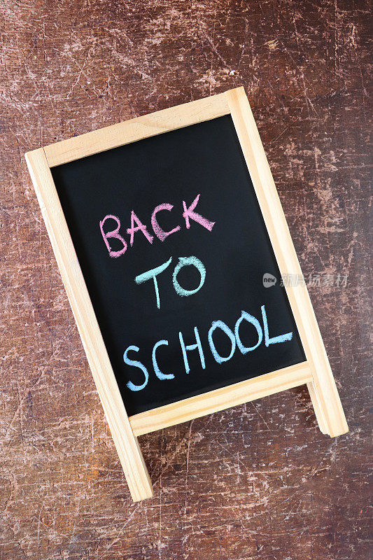木制a框板黑板图像，粉色、蓝色和绿色粉笔用大写字母写着“回到学校”的标题，棕色背景，抬高视图