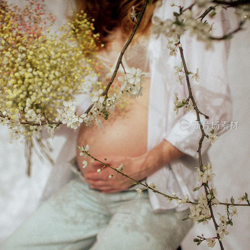 女人的手抚摸着她怀孕的肚子，上面映着花朵的影子。