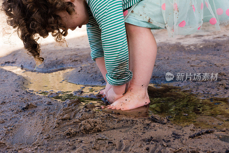 光着脚蹒跚学步的孩子在沙子和水里玩耍