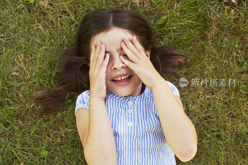 年轻的女孩躺在草地上遮住眼睛