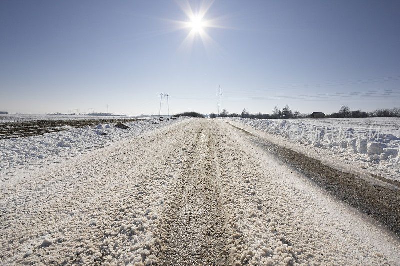 阳光明媚的冬日里，白雪覆盖的柏油路穿过乡间