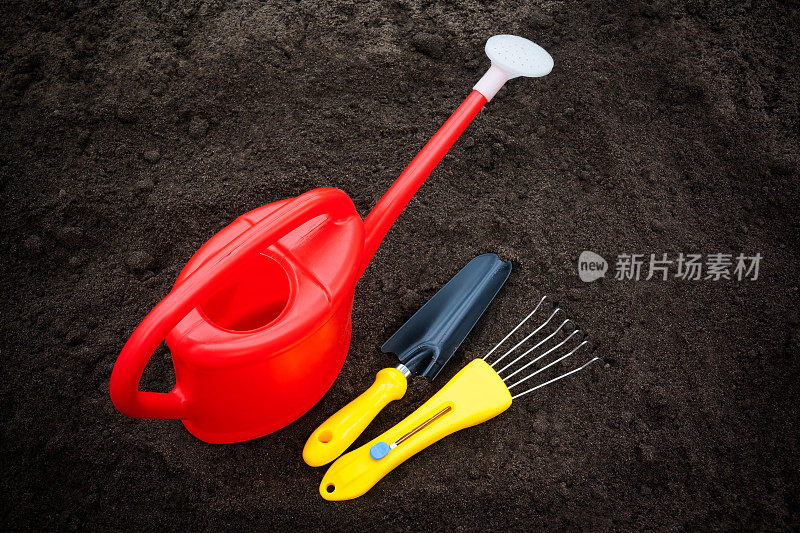 红色喷壶，耙子和铲子在土壤上