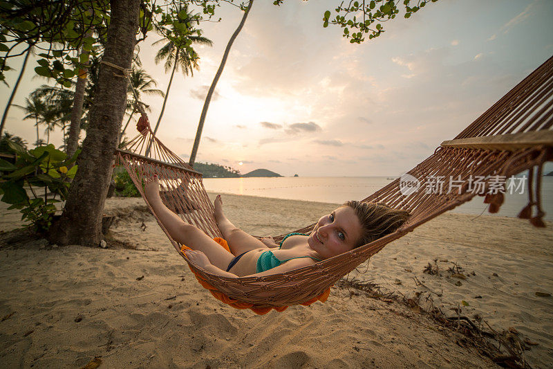 一个快活的年轻女子躺在吊床上，欣赏着日落