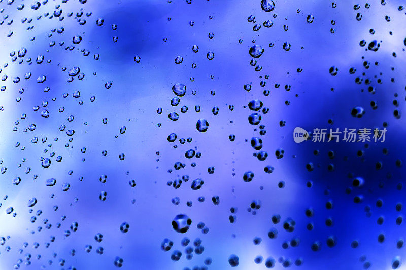 雨点落在玻璃窗上。蓝色背景。