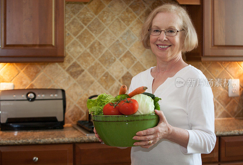 年长的女人在厨房里端着一碗新鲜的蔬菜
