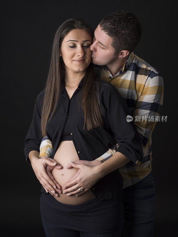 一对夫妇的手在怀孕的腹部做心形的肖像