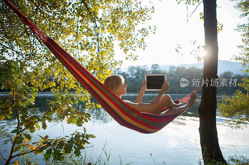 日落时分，一名女子在吊床上用平板电脑拍照