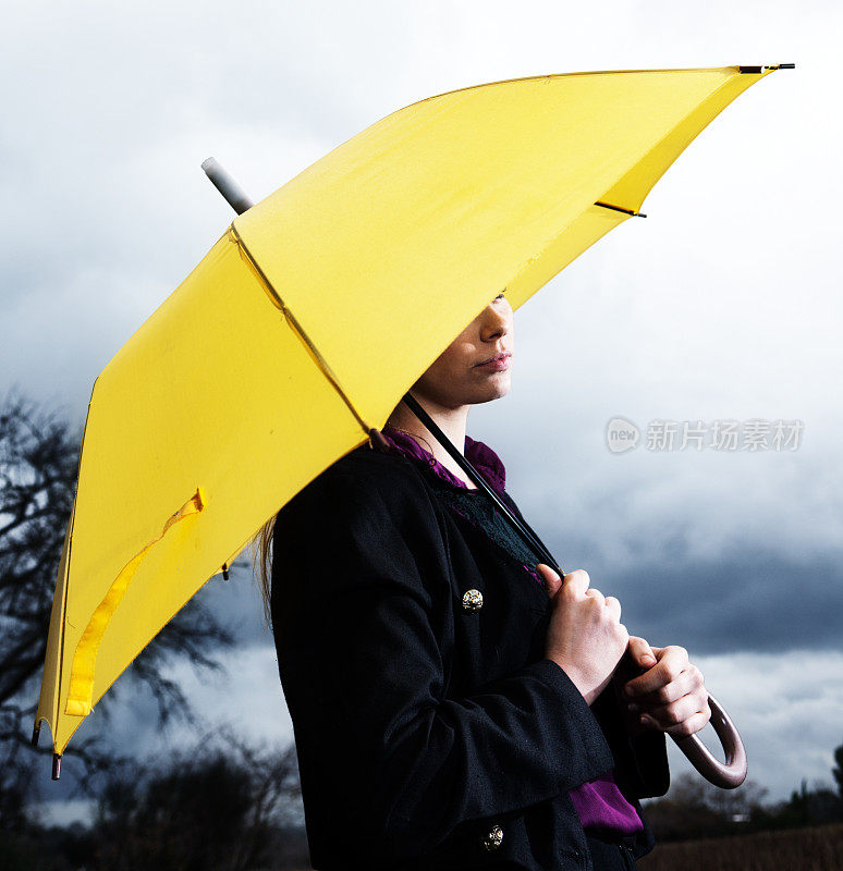美丽的金发女郎在暴风雨中躲在伞下