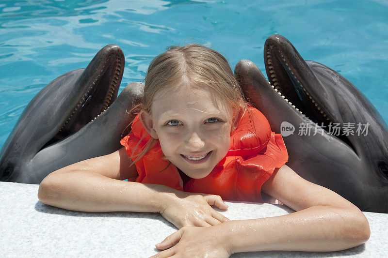 快乐的小女孩和两只海豚在游泳池里。