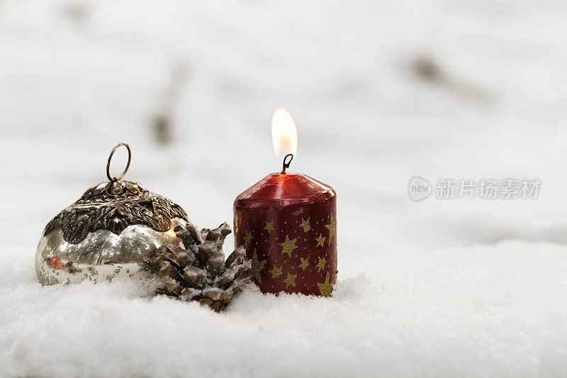 燃烧的蜡烛，圣诞的小装饰品和松果在雪中