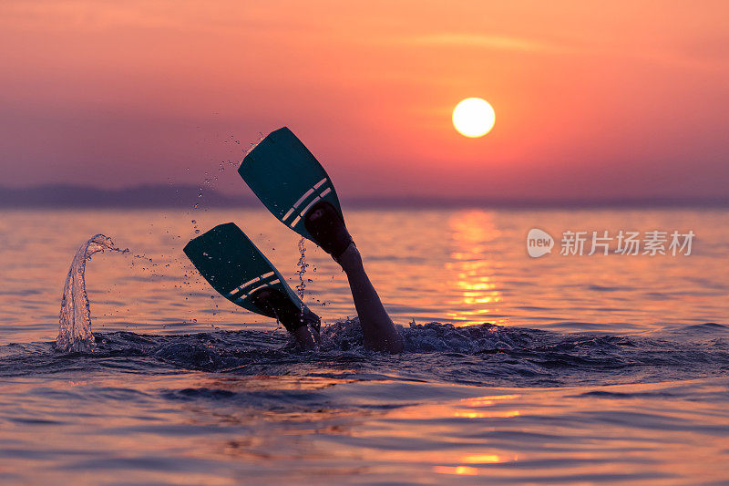 日落时在海面上穿着鳍状肢的潜水员