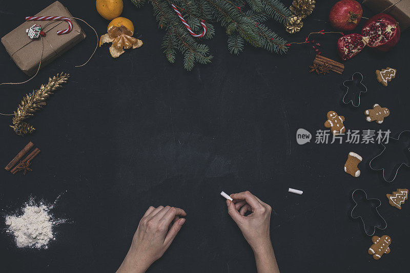 圣诞节的背景。俯视图女人的手写在粉笔牌子上。黑色的桌子上放着包装好的礼物和云杉树枝。准备手工新年装饰品的工作场所。