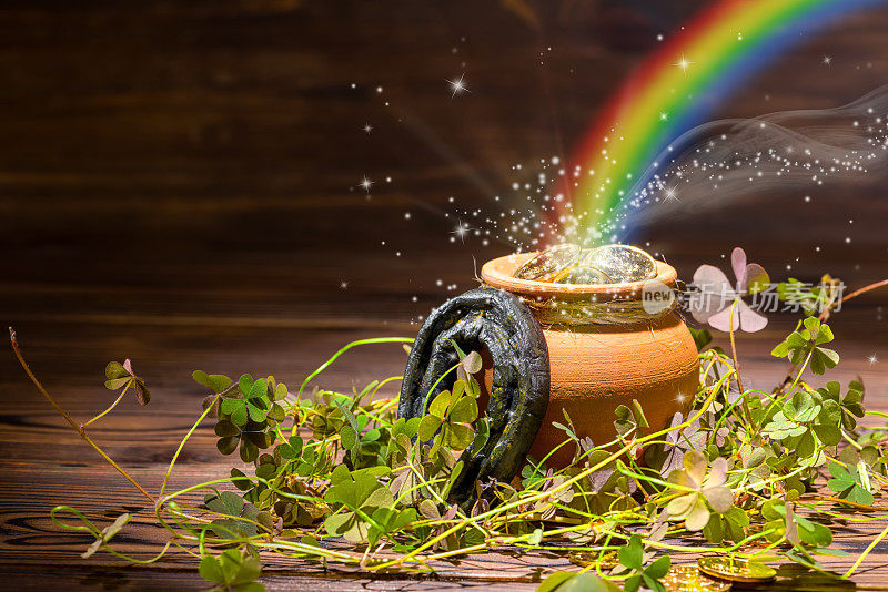 圣帕特里克节装饰用魔法光彩虹壶满金币，马蹄和三叶草在复古木制背景，近
