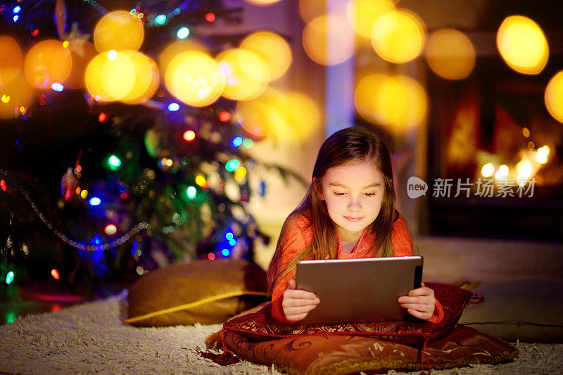 可爱的小女孩在圣诞节晚上壁炉边使用平板电脑