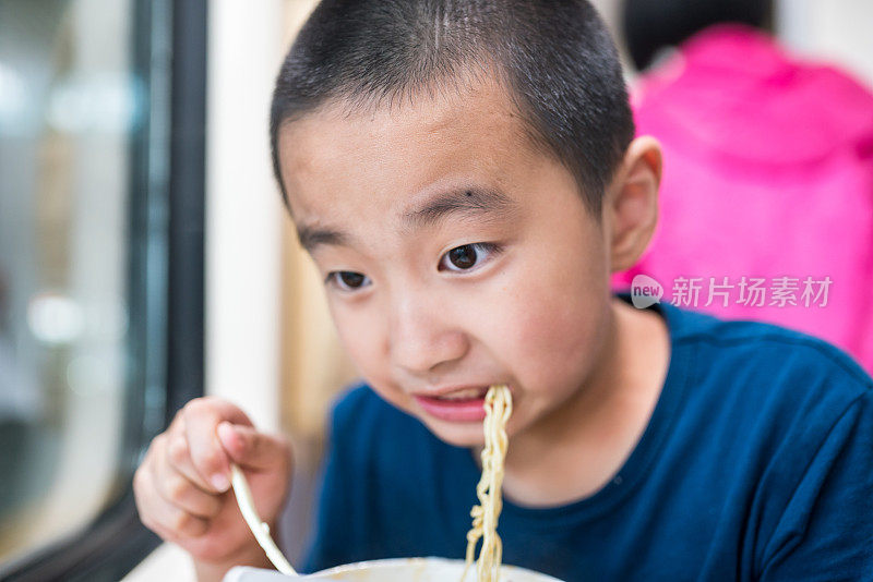 亚洲男孩乘火车旅行，吃着方便面