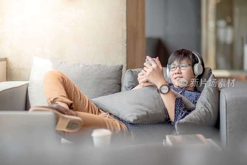 年轻的亚洲男子在沙发上使用智能手机