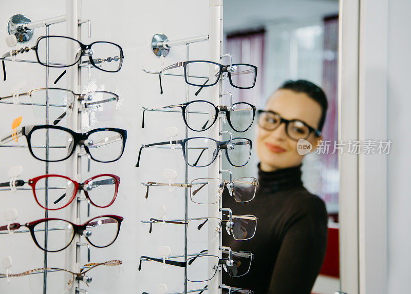 和眼镜一起站在光学商店。背景是一个戴眼镜的漂亮女孩。有选择性的重点