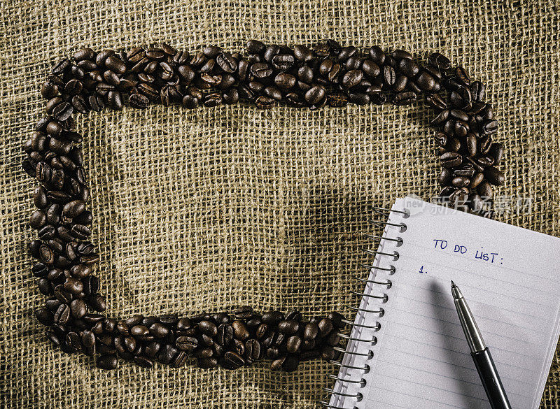 烤生咖啡豆制作框架在黄麻背景与笔记本做清单