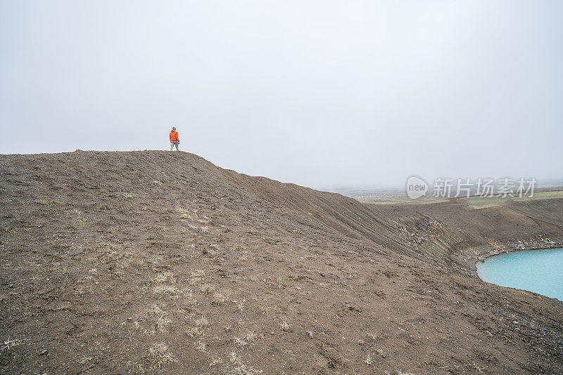 远处的人行走在冰岛火山口的山脊上，雾气缭绕