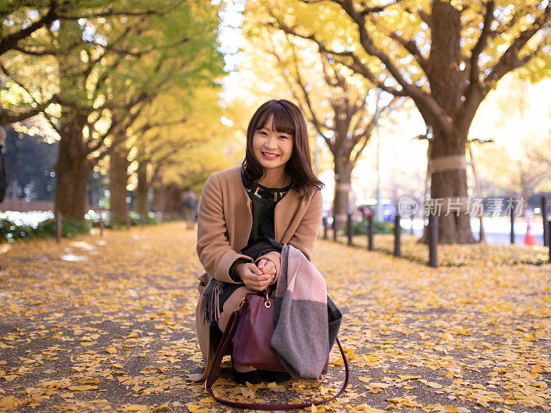 一名年轻女子坐在满是银杏叶的街道上的肖像