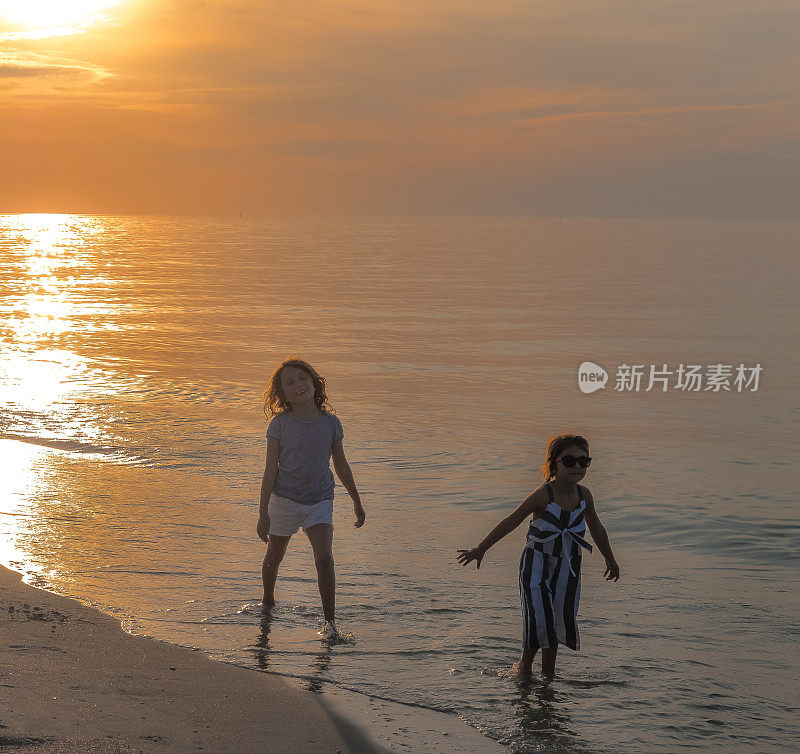 酷酷的孩子们，戴着墨镜的小女孩和一个姐妹或朋友在海边沙滩上奔跑，快乐，看起来很酷，而且充满活力