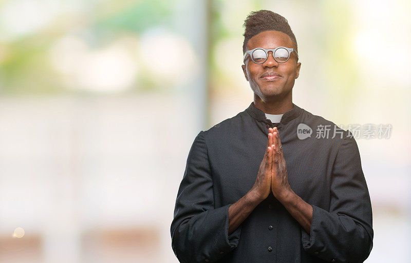 年轻的非洲裔美国牧师在孤立的背景下双手一起祈祷，自信地微笑着请求宽恕。