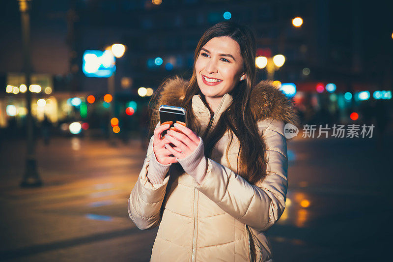 年轻女子晚上在城市里使用智能手机