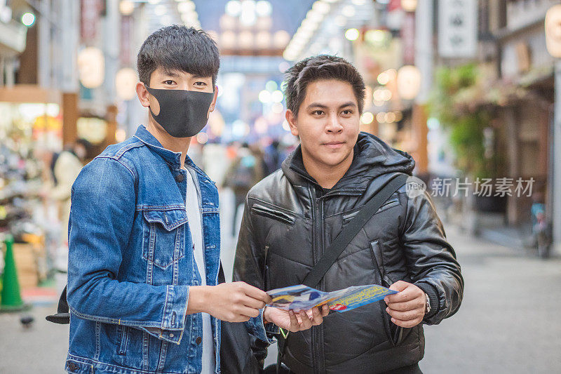 年轻的亚洲男子和日本朋友寻找旅游地点使用手机和花时间在亚洲旅行