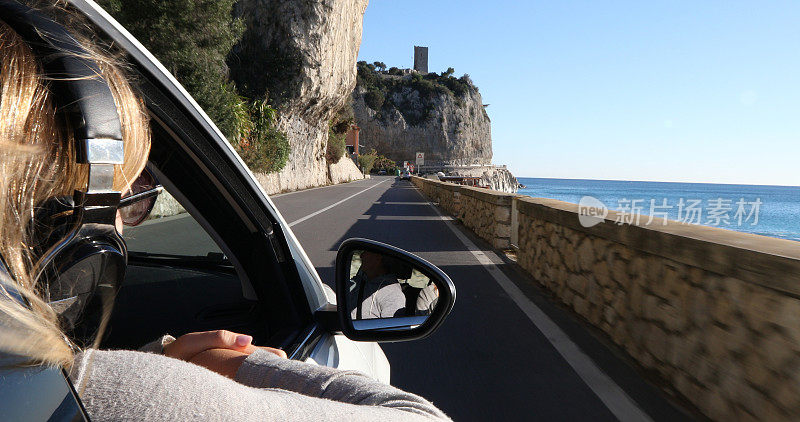 一名年轻女子开车沿海岸线旅行时听着耳机