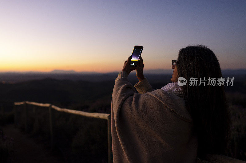 一名女子登上山顶，用手机拍照