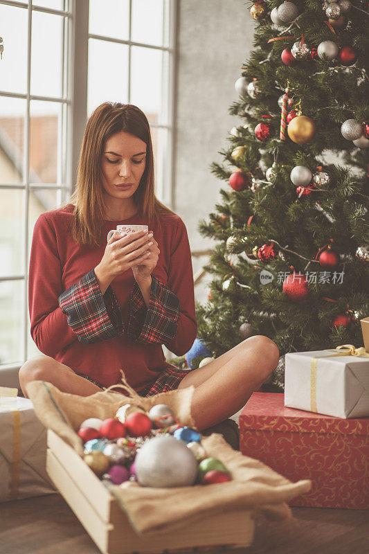 女人放松与一杯热茶在她的圣诞树旁