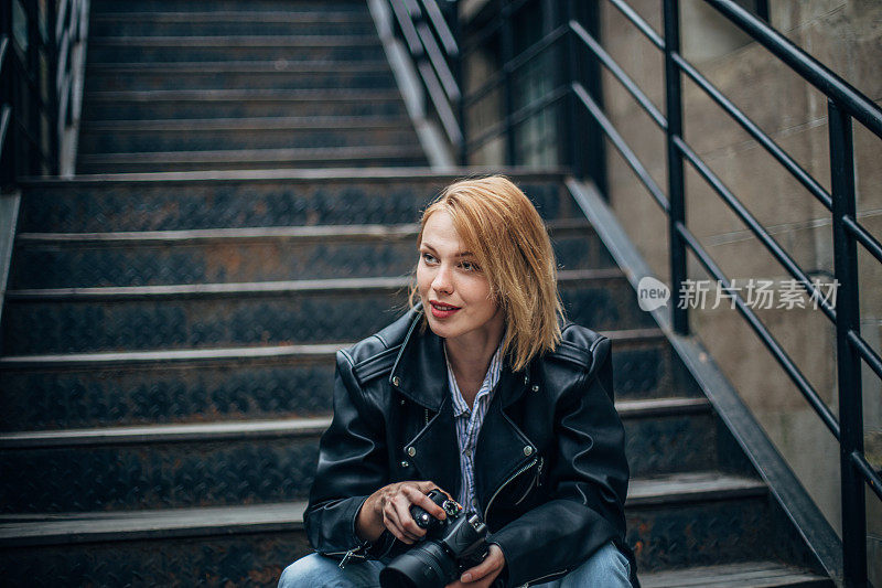 金发女摄影师坐在城市的台阶上