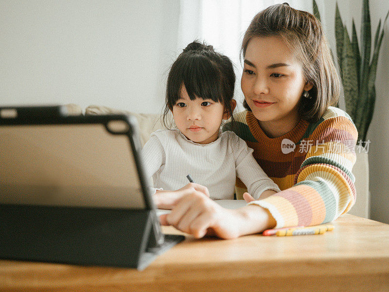 年轻的母亲和女儿在家里用平板电脑做作业。