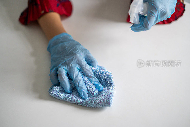 年轻妇女戴上手套，用清洁布和消毒剂喷雾清洁桌子表面