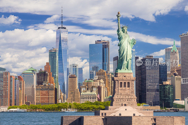 自由女神像和纽约天际线，曼哈顿金融区，世界贸易中心，纽约港水，炮台公园和蓝天。