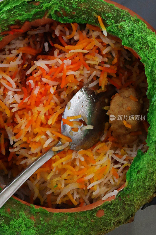近距离的图像赤陶罐与金属勺子包含印度外卖米饭，鸡肉biryani与鸡masala肉汁酱在玻璃桌上