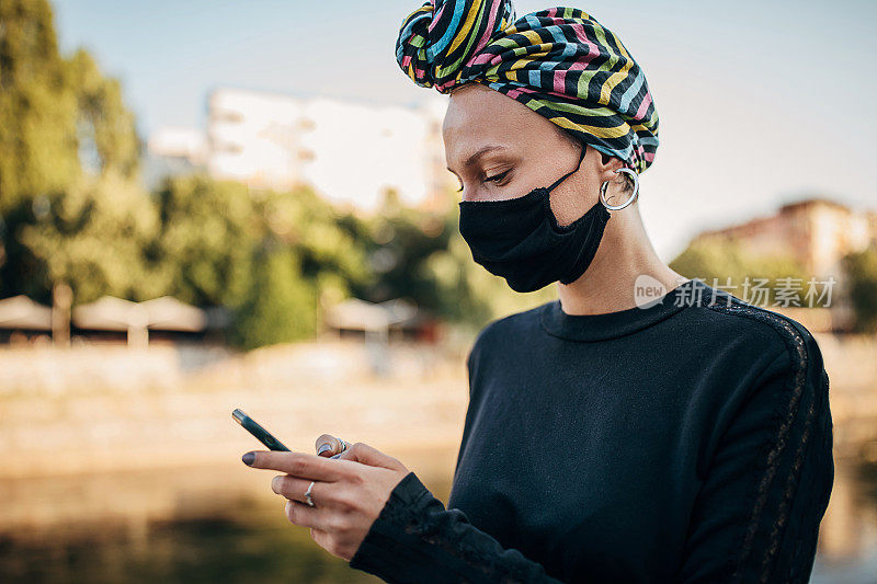 一名妇女戴着头巾和防护口罩使用智能手机