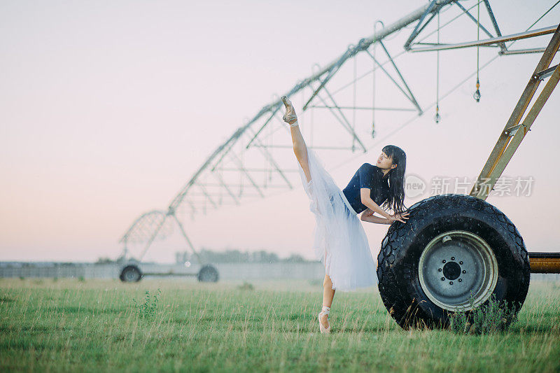 一名芭蕾舞演员在农用喷雾器的轮子旁边表演燕子姿势。