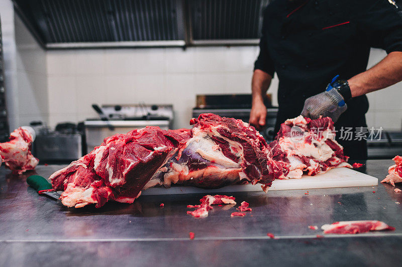 男屠夫在餐厅厨房用刀切生牛肉