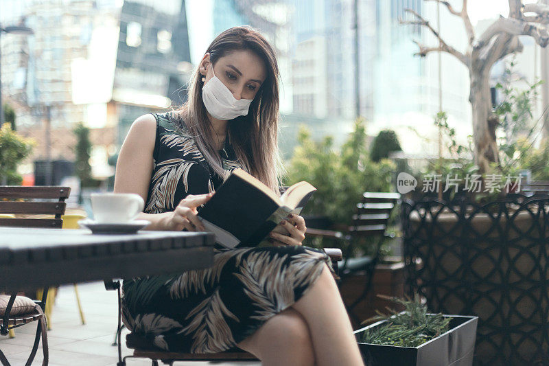 年轻女子戴着防护口罩，在咖啡馆看书