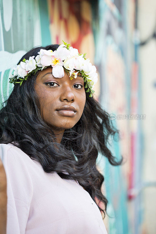 一个自信的年轻女子，头发上插着鲜花，头发被风吹着，站在市中心的涂鸦前