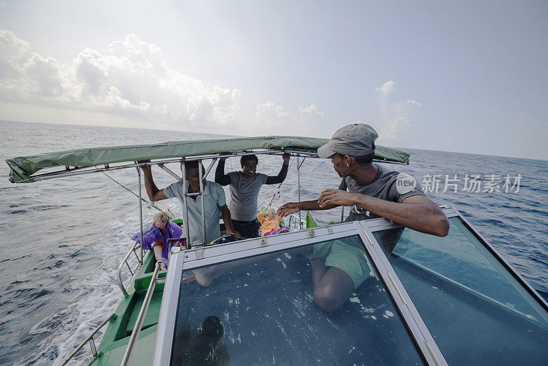 一名船长在一艘小渔船的甲板上休息，两个渔民，船员，正在与游客，欧洲妇女交谈，她们在后面休息，等待咬一口。