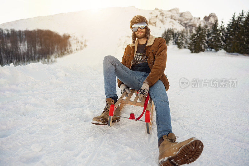 一个戴着滑雪眼镜坐在雪橇上的年轻人