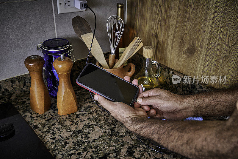 在家庭厨房里，一名男子用手将充电电缆连接到智能手机上