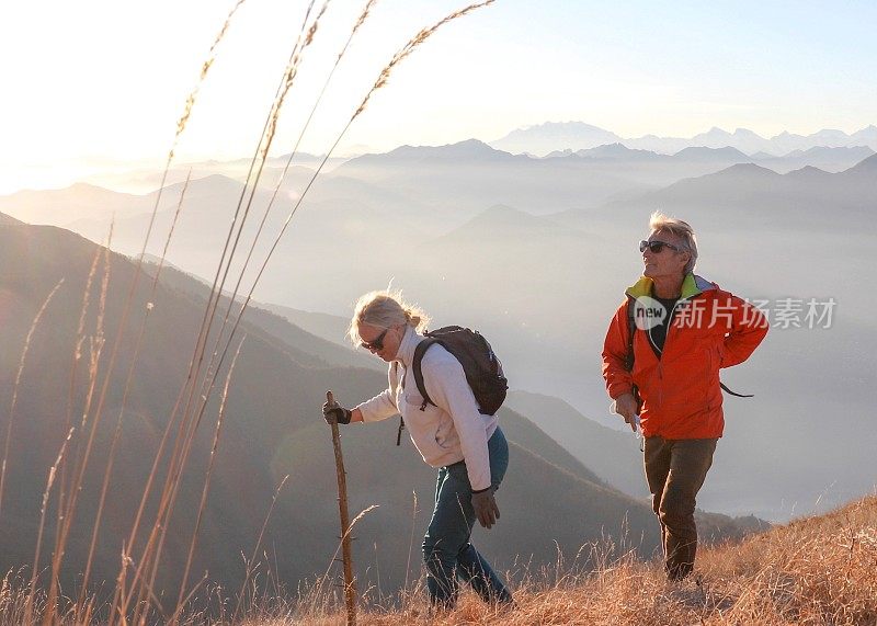 一对成熟的夫妇早晨沿着长满草的山坡徒步旅行