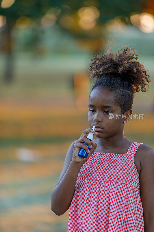 过敏的可爱的卷发小女孩正在公园里喷鼻喷雾。