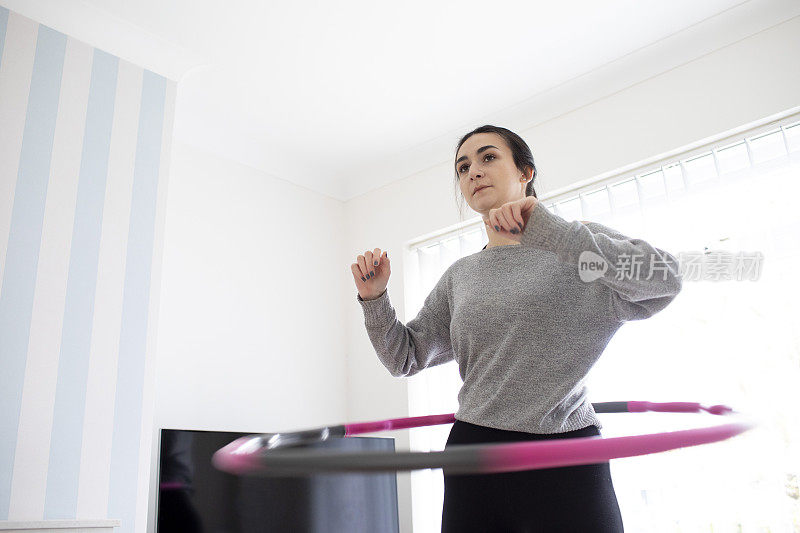 一名年轻女子在一所房子的起居室窗前用呼啦圈练习